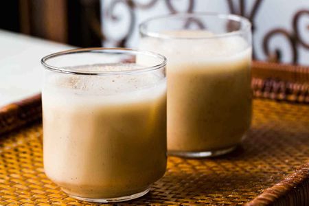 Two glasses of creamy Coquito on a woven mat