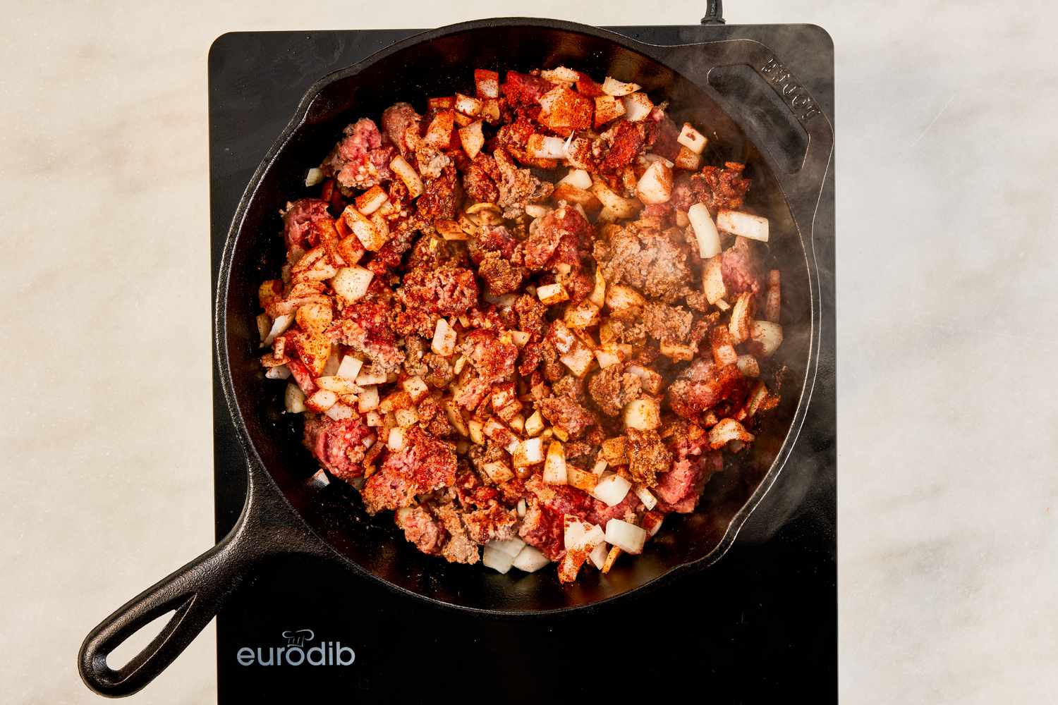 ground beef, onions, and seasoning cooking in a cast iron skillet for crispy ground beef recipe