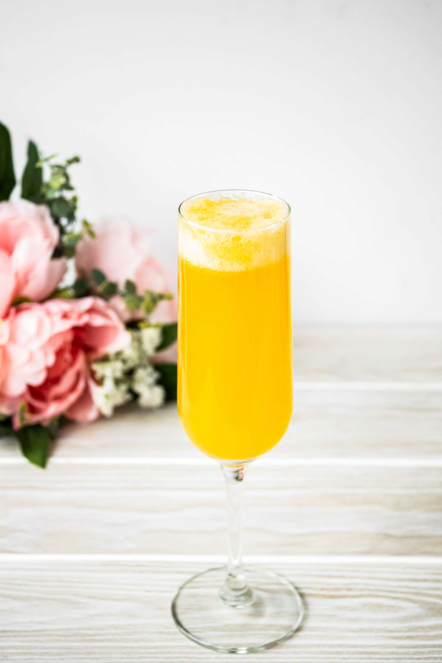 Flute of Peach Belini Cocktail with Flowers in the Background
