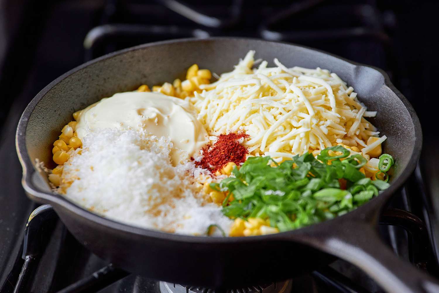 Corn Kernels, Cheeses, Mayonnaise, Gochugaru, and Green Onions Added to a Cast Iron Skillet on the Stove for Korean BBQ Cheese Corn