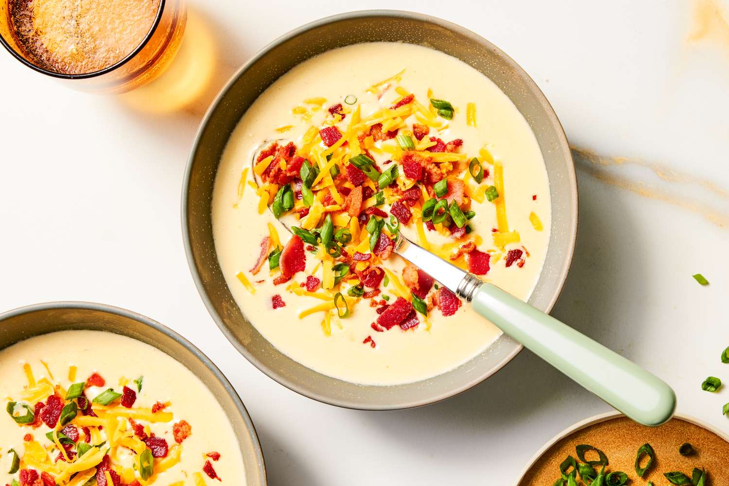 A bowl of loaded potato soup garnished with shredded cheese bacon bits and green onions with a spoon placed inside