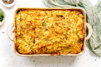Potato Kugel in a Casserole Dish Surrounded by a Small Saucer with Herbs, Another Small Saucer with Cracked Pepper, and a Kitchen Linen
