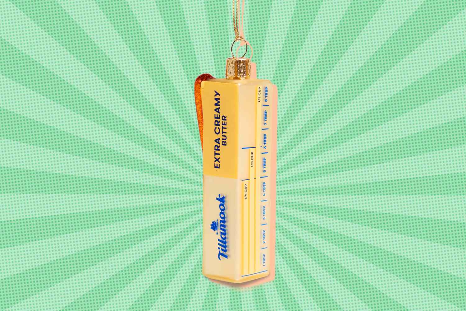 A novelty Christmas ornament shaped like a stick of butter hanging with a green background