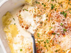 Casserole dish with a creamy layered casserole topped with grated cheese and parsley part of the dish served with a spoon