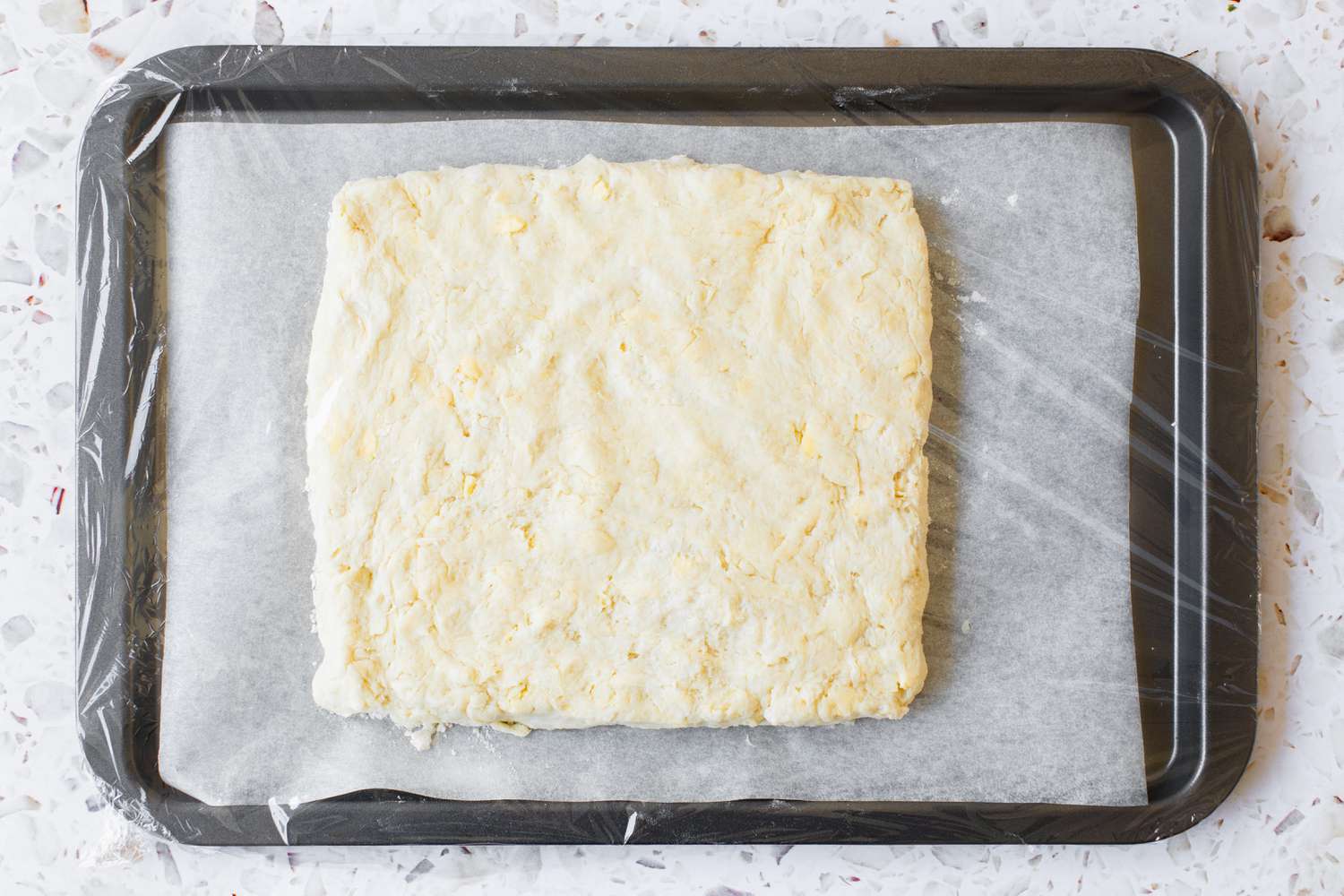 Strawberry Shortcake Biscuit Dough Formed into a Square, Placed on a Parchment Paper Lined Baking Sheet, and Covered in Plastic Wrap 