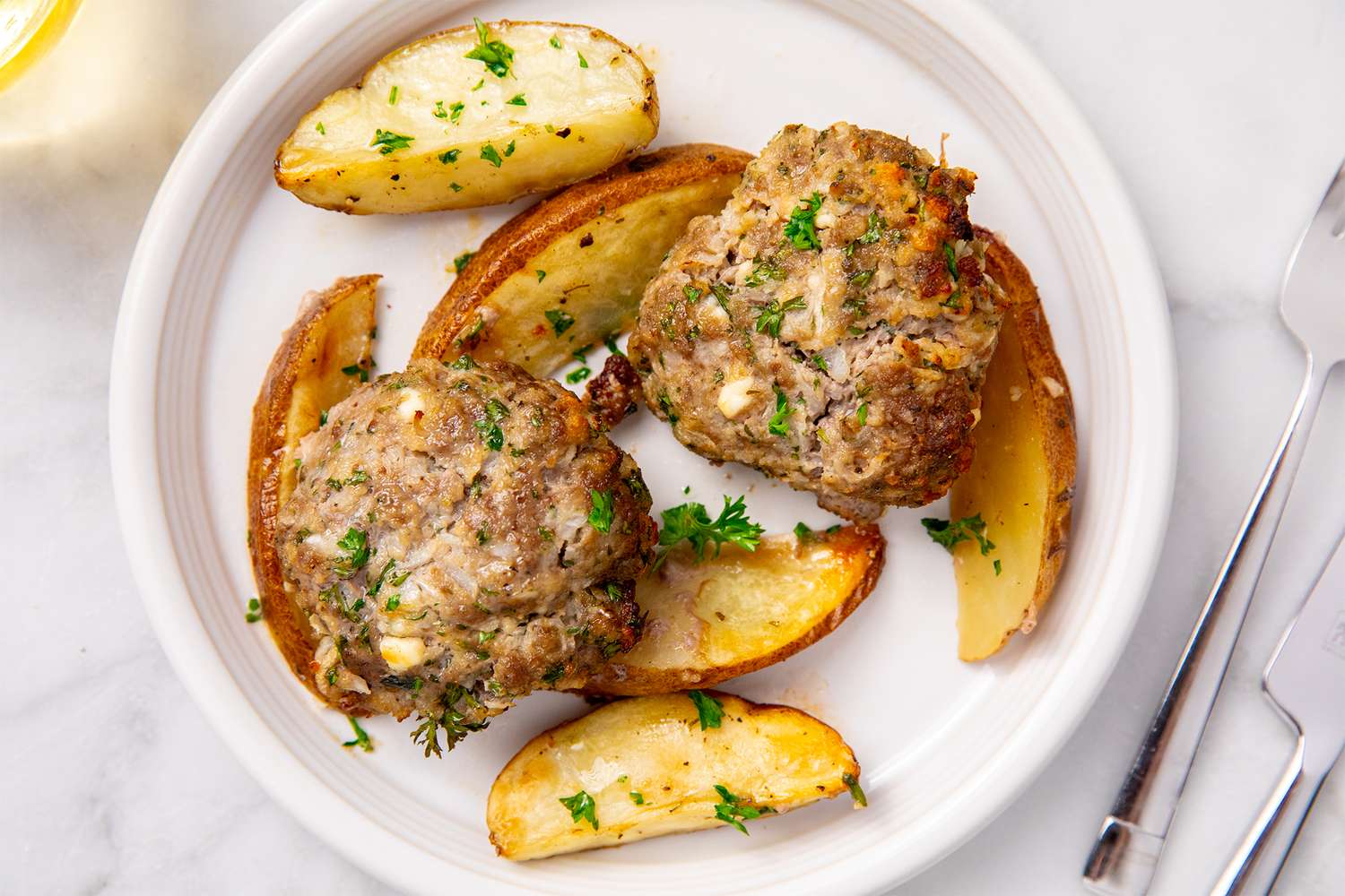 A plate featuring meat patties with potato wedges and garnish
