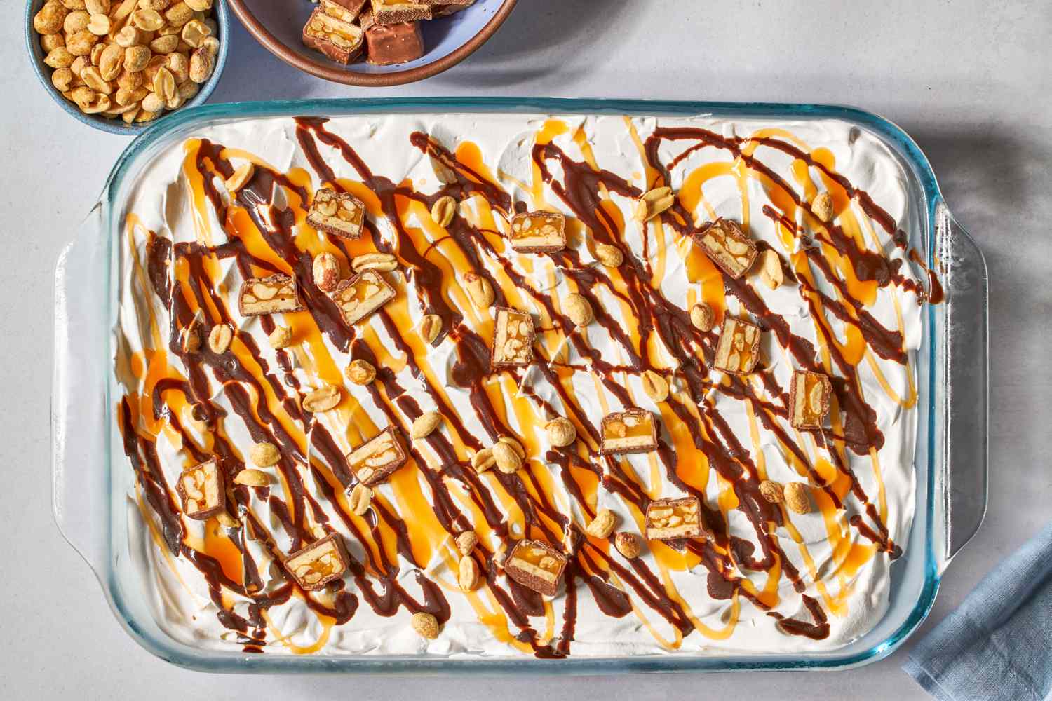 Glass dish of snickers ice cream casserole with caramel and chocolate drizzle, garnished with peanuts and candy pieces