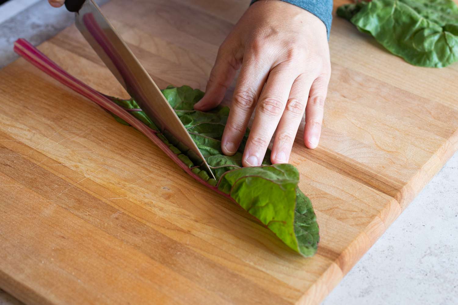 Folded chard leaf on cutting board knife cutting it away
