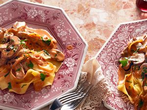Two plates of beef stroganoff served over wide noodles garnished with herbs