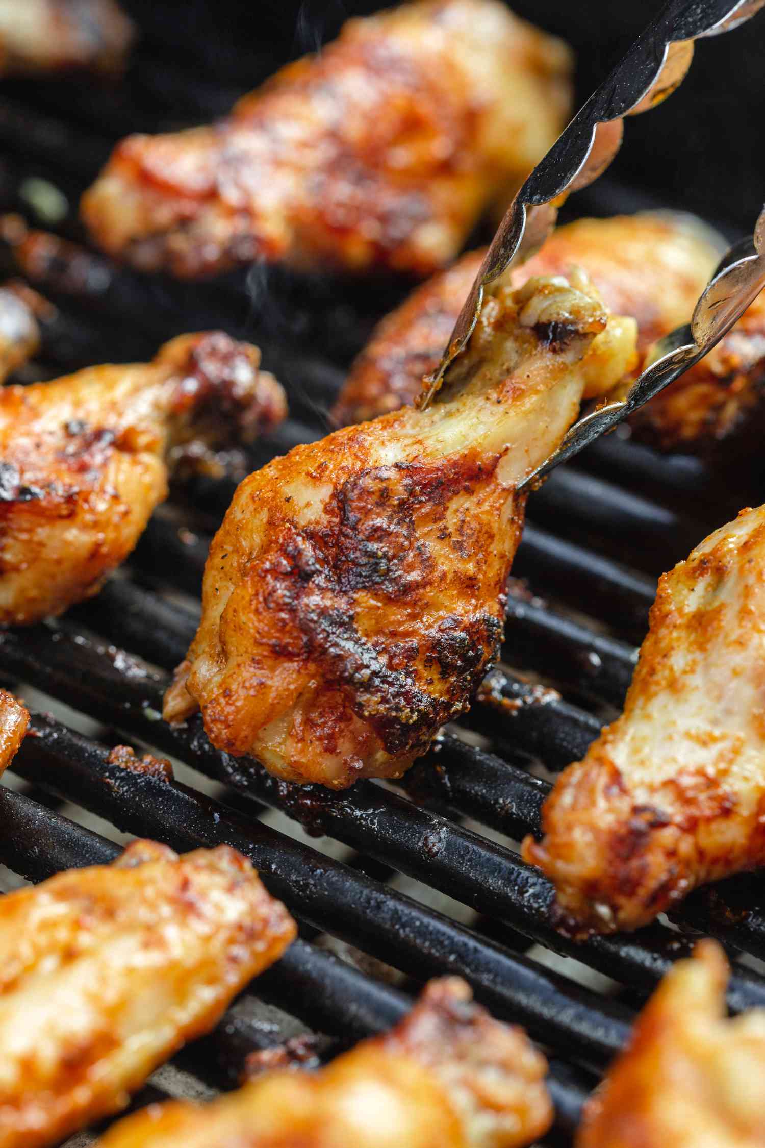 Tongs picking a bbq chicken wing up off the grill.