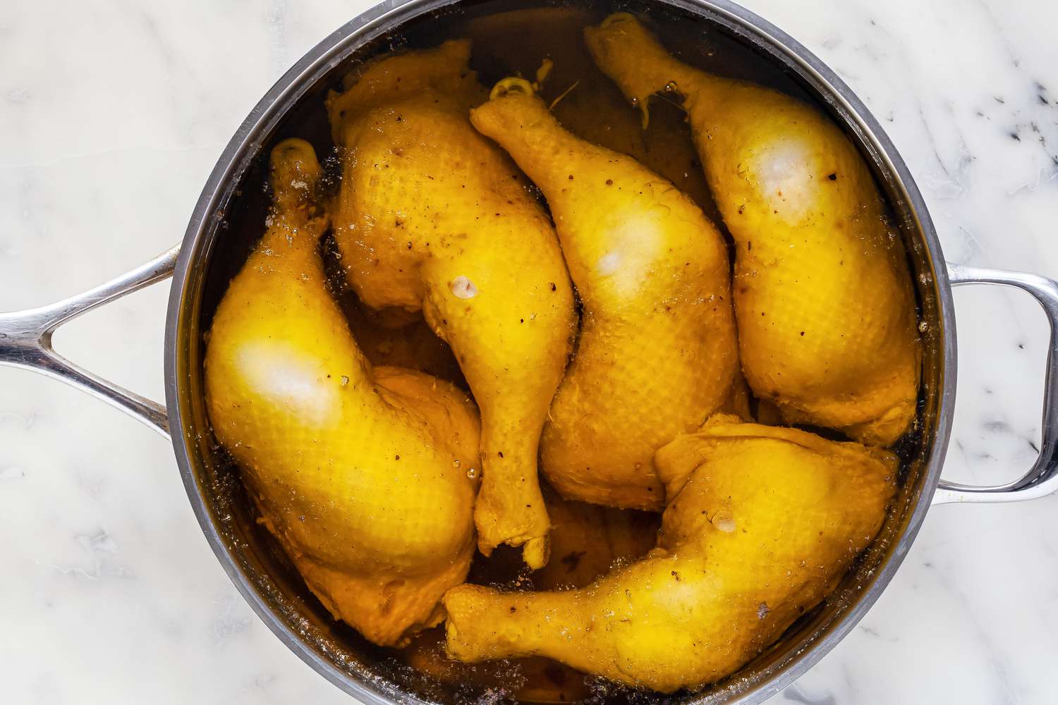 Whole chicken legs simmering in olive oil.