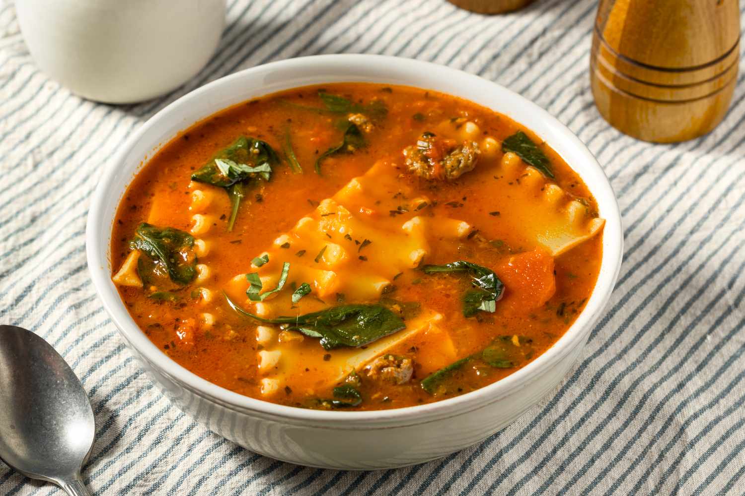 Bowl of tomato soup with lasagna noodles spinach and a striped tablecloth