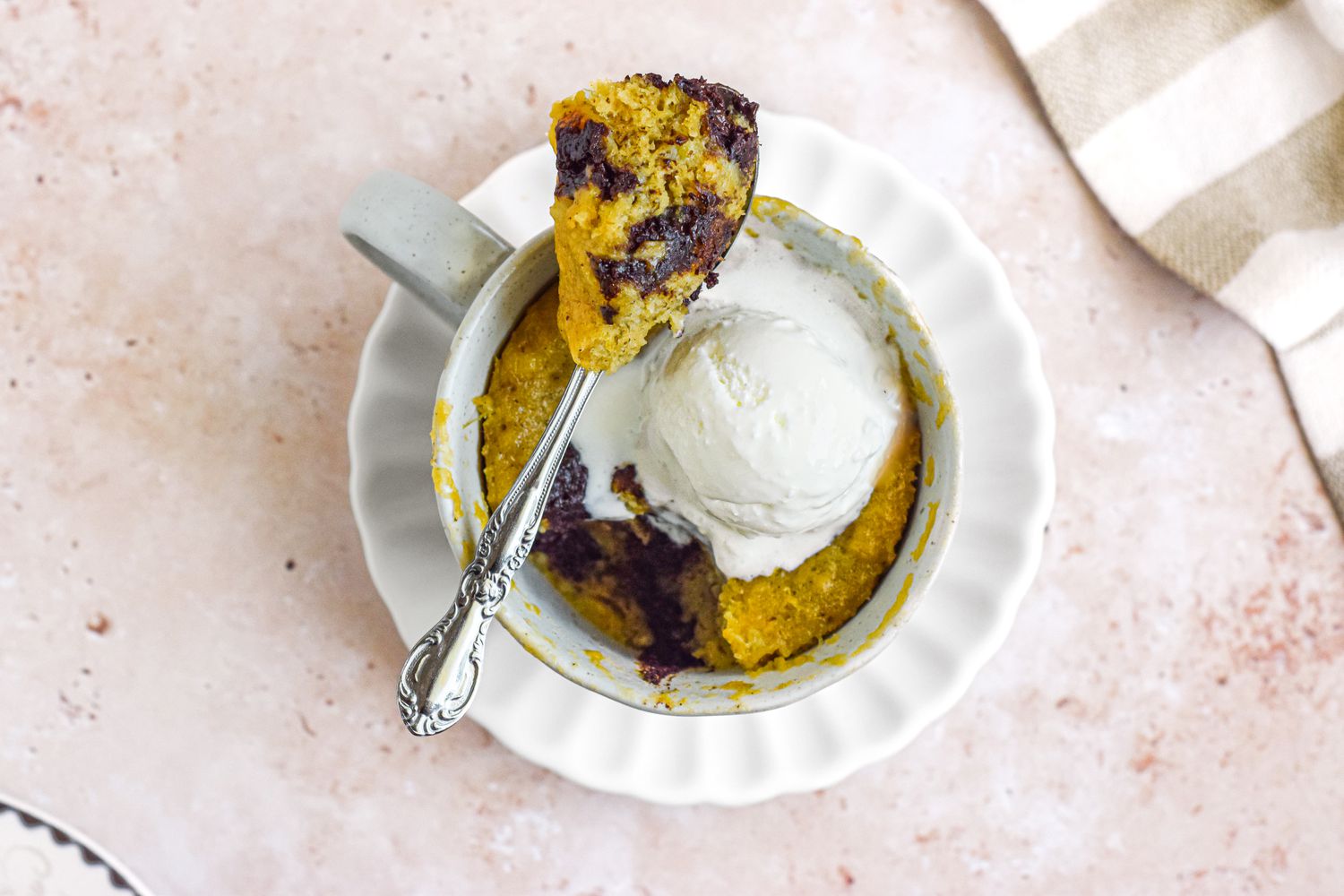 Mug of Banana Bread Chocolate Chunk Mug Cake Topped with a Dollop of Ice Cream and Spoonful of Cake Resting on Top of the Mug