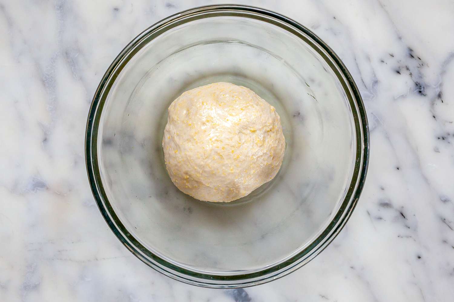 Dough rising in a glass bowl to make Homemade Chicago-Style Deep Dish Pizza.
