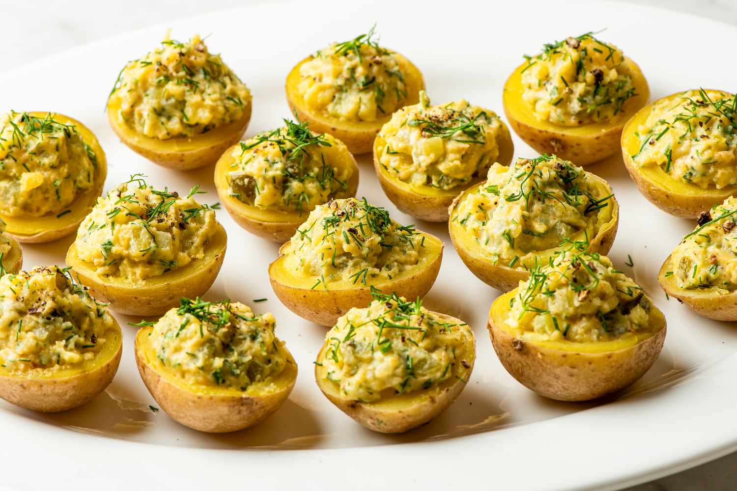 Plate of deviled potatoes garnished with dill and herbs arranged in rows on a white serving platter