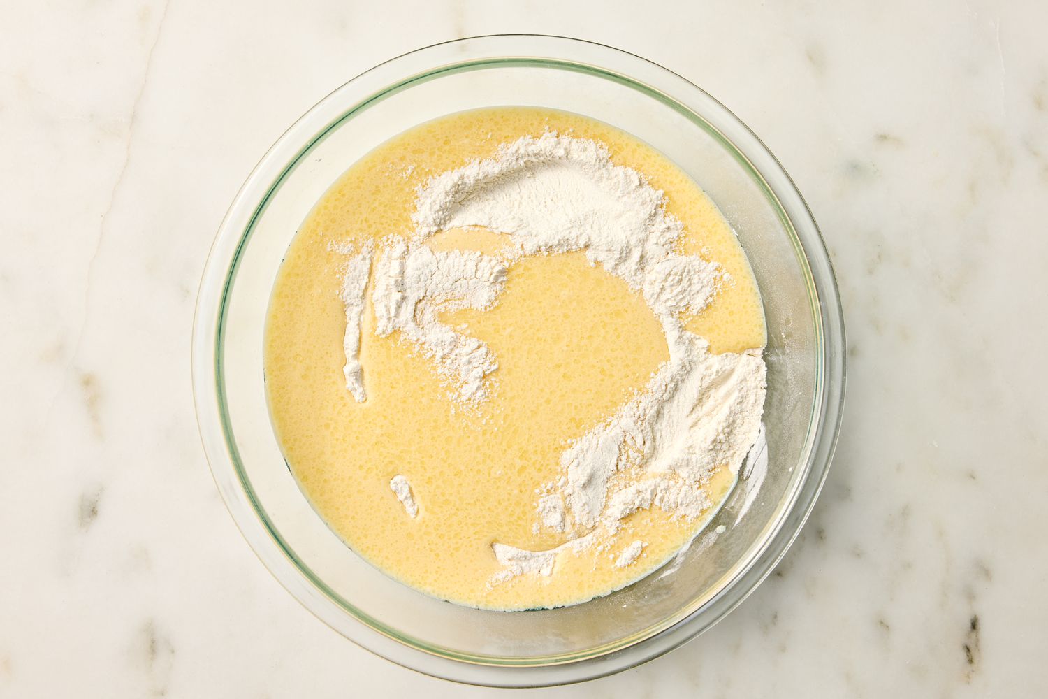 A mixing bowl containing a partially mixed cake batter with visible flour on top from Easy Vanilla Cake recipe