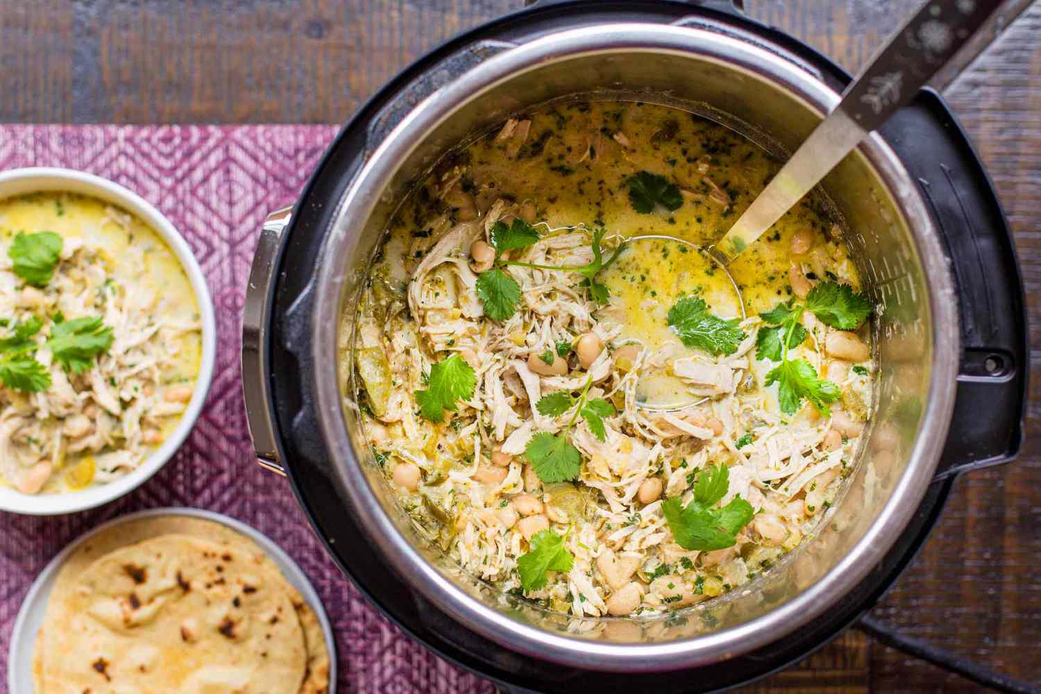 An instant pot filled with white chicken chili garnished with herbs two small bowls of similar chili and some tortillas on the side