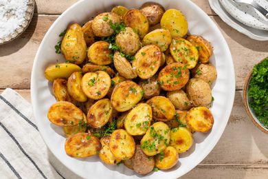 Roasted halved potatoes in a large white serving bowl, sprinkled with flakey salt and parsley