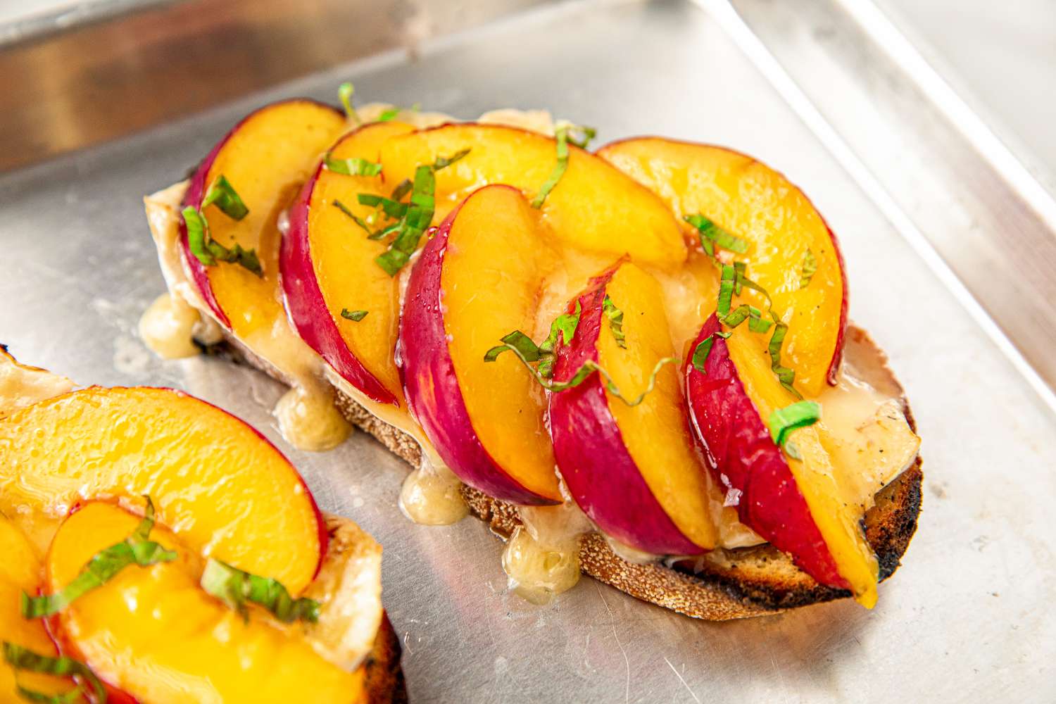 Slices of nectarine and melted brie on toasted bread garnished with fresh herbs