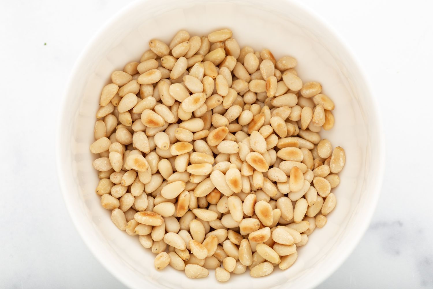 Toasted pine nuts in a bowl for a pesto pasta salad recipe.