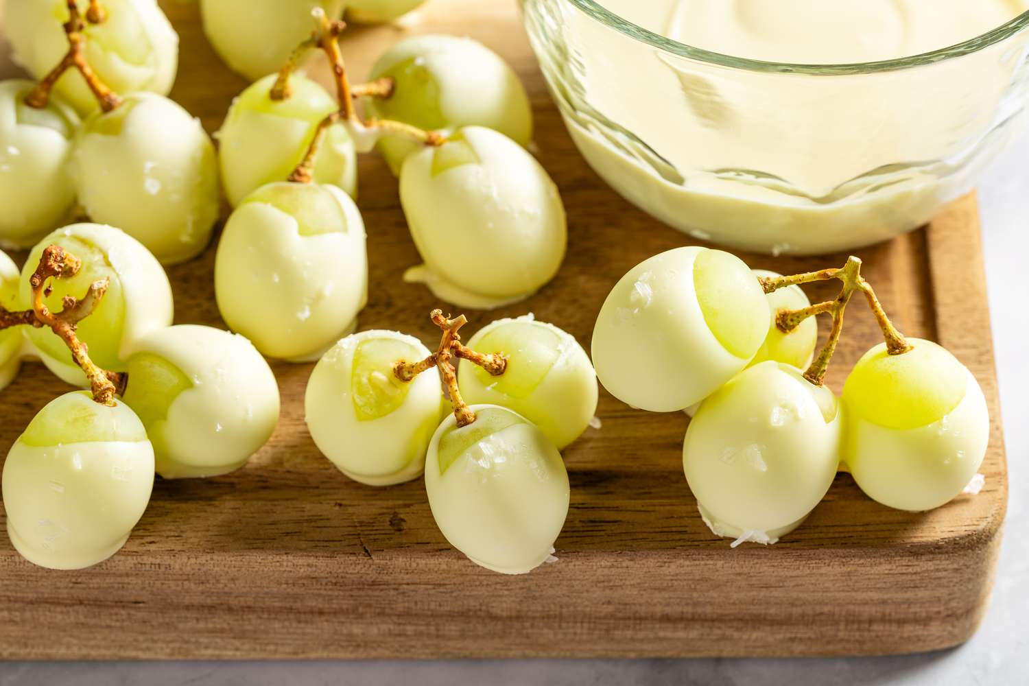 Closeup view of white chocolate covered green grapes on a wooden cutting board on a gray countertop