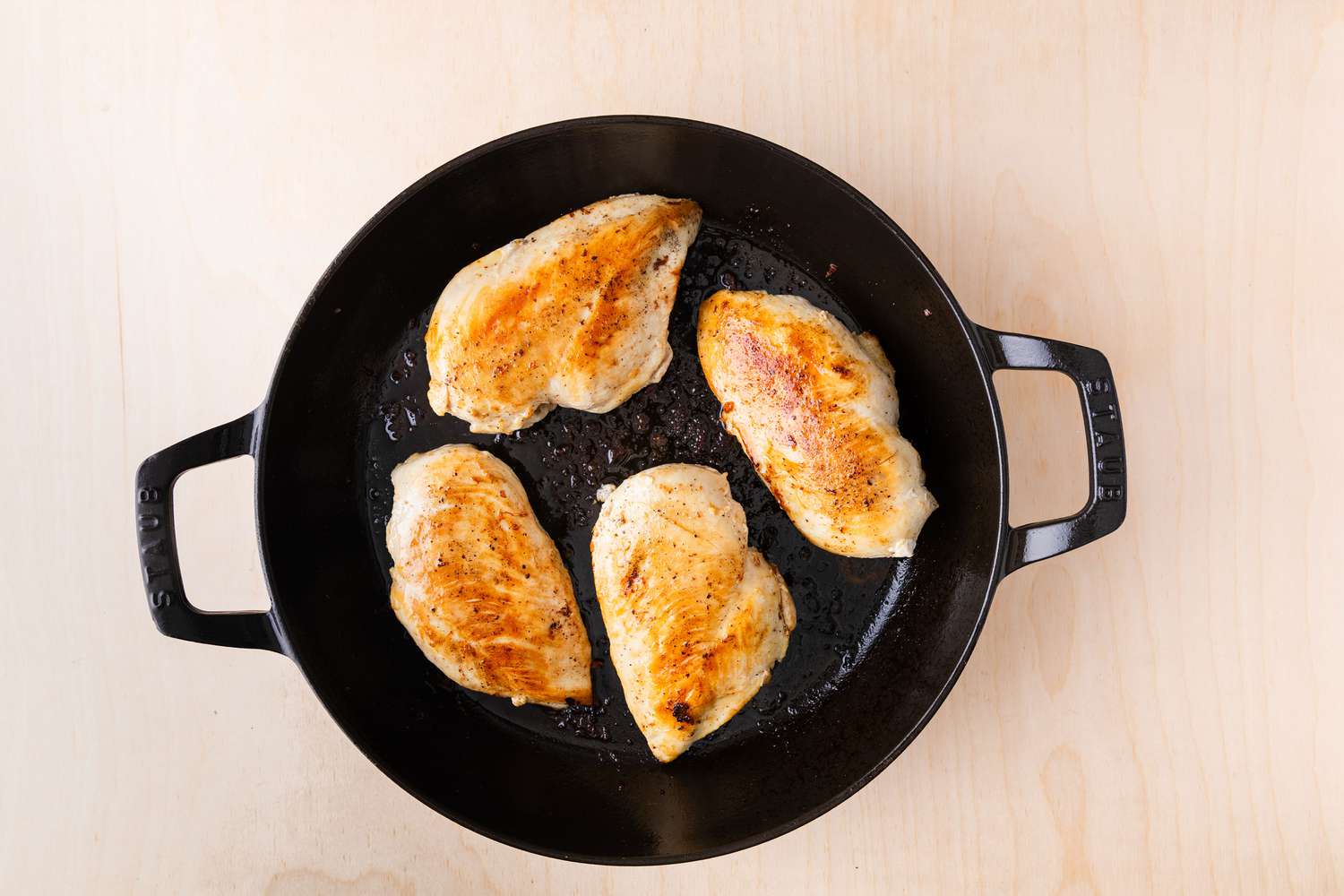 Four boneless, skinless chicken breasts, browned on top and cooking in a large cast iron skillet