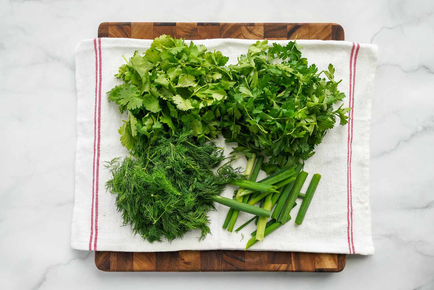 Fresh Cilantro, Parsley, Dill, and Green Onions on a Kitchen Towel Over a Cutting Board for Persian Herb Rice Recipe