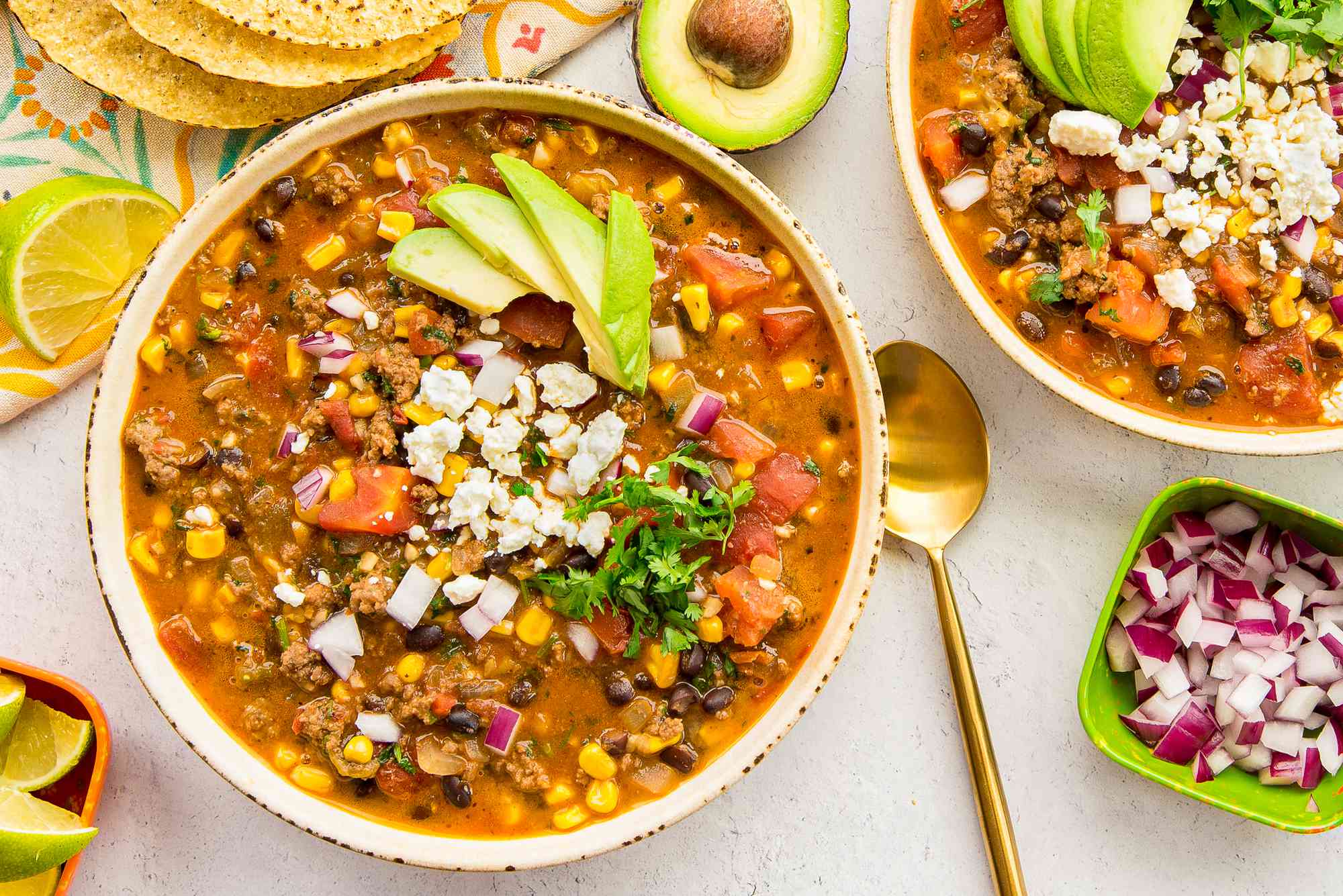 Stovetop Taco Soup in a Bowl Topped with Avocado Slices, Cotija Cheese, and Cilantro and Surrounded by Bowls of Toppings