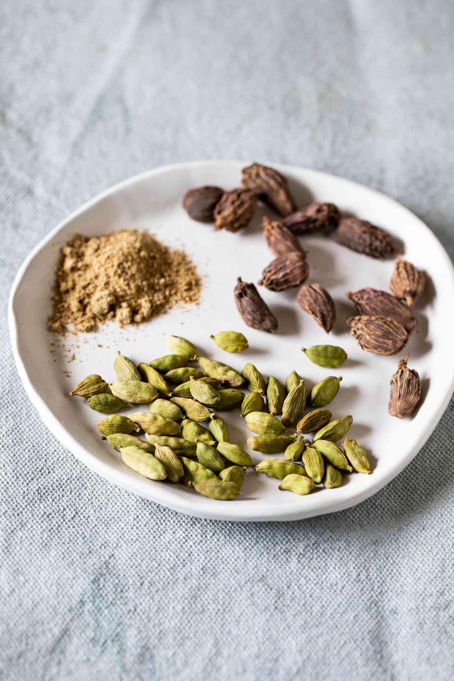 Ground cardamom and green and brown cardamom pods on a white plate