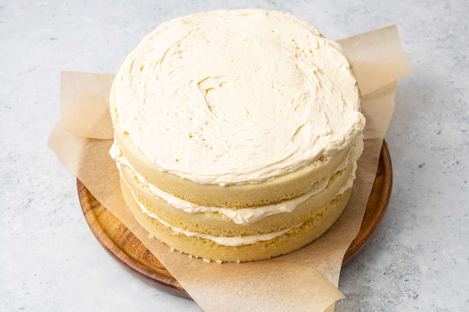 3-Layer Cake In the Microwave Assembled with Layers of Cake and Frosting on a Parchment Paper Lined Wooden Plate