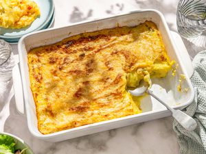 A white casserole dish with Irish baked mashed potatoes, with part of the dish scooped out, on a white marble counter