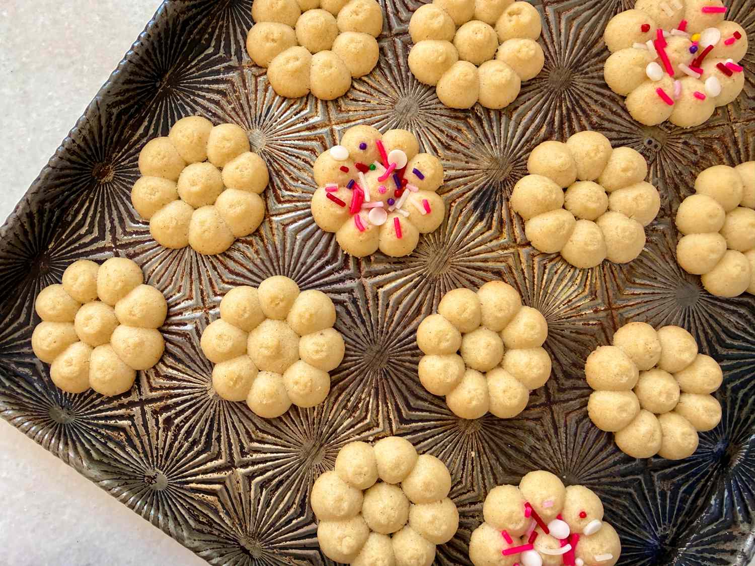 A tray of flowershaped cookies some decorated with sprinkles