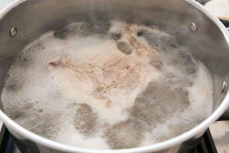 Boiling a chicken to show how to make chicken noodle soup.