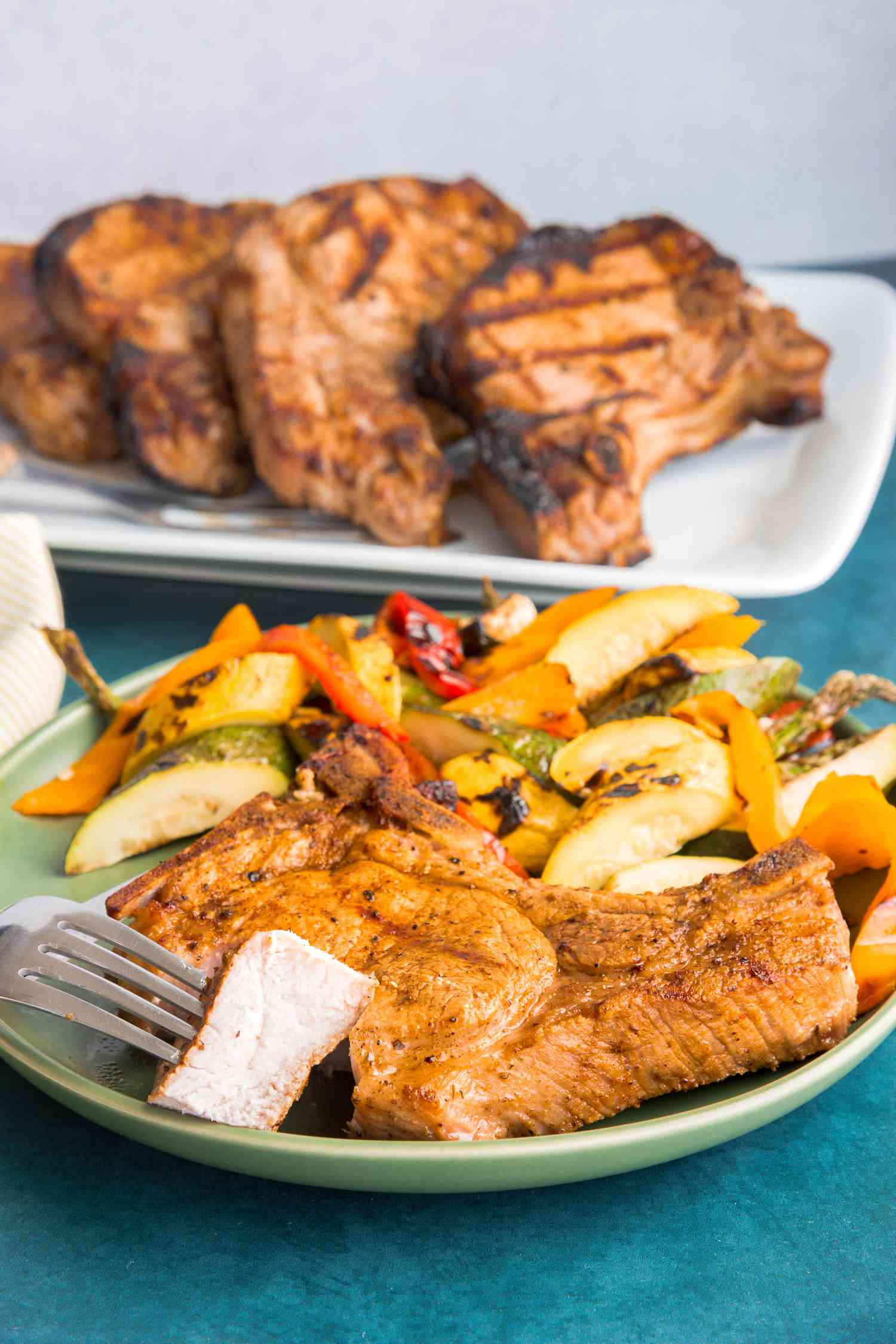 Grilled Pork Chops on a Plate with Piece on Fork and Platter of Pork Chops in Background