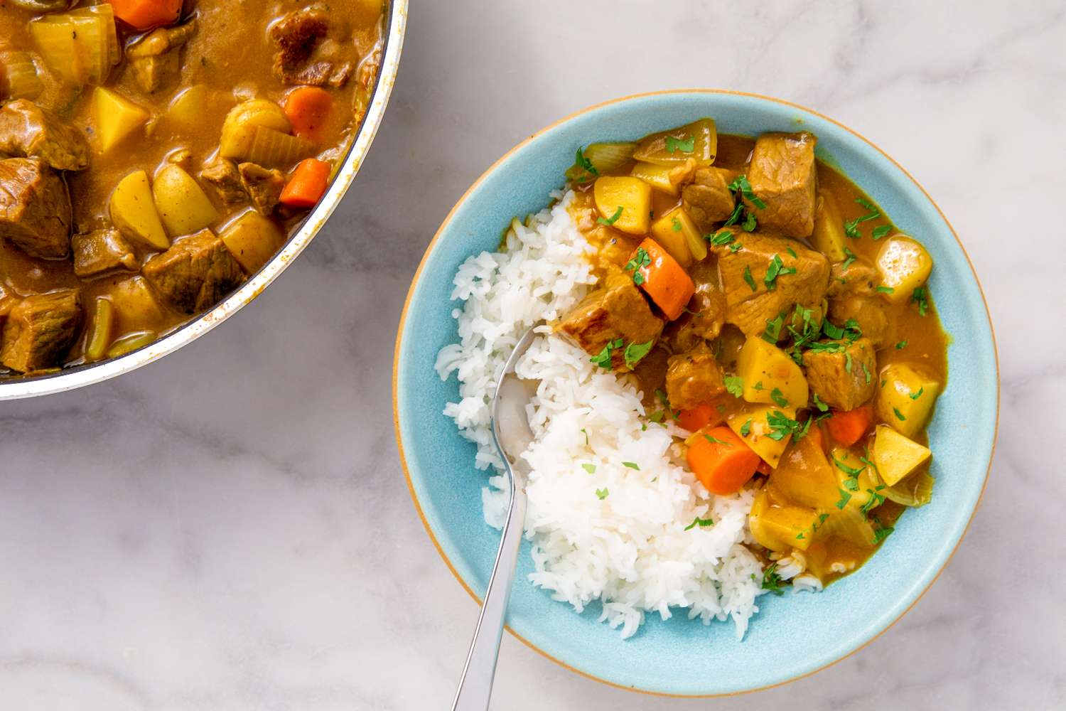 A bowl of Japanese curry with vegetables and rice placed next to a pot filled with the same curry