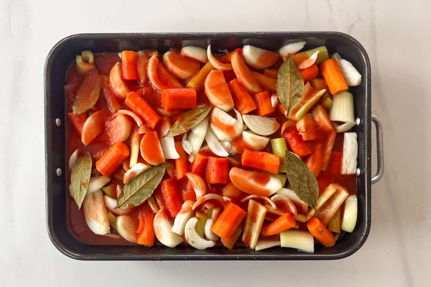 A roasting pan filled with chopped vegetables bay leaves and a sauce prepared for cooking brisket