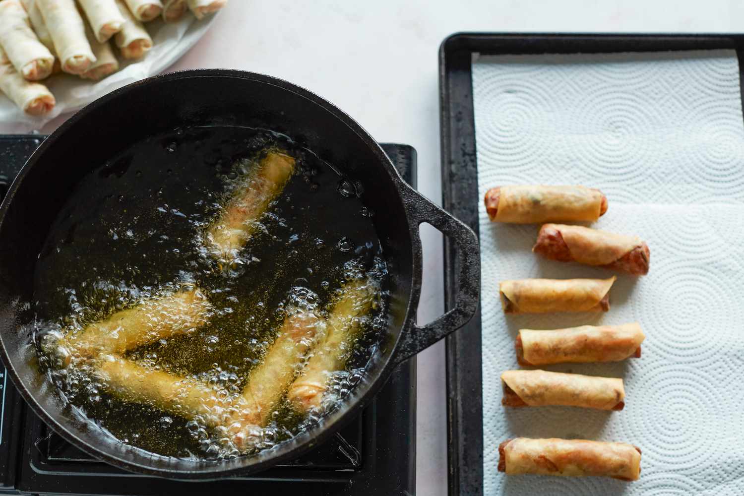 Overhead view of spring rolls frying in a skillet.