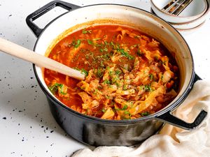 Pot of Sweet and Sour Cabbage Soup Next to a Kitchen Linen and a Stack of Bowls