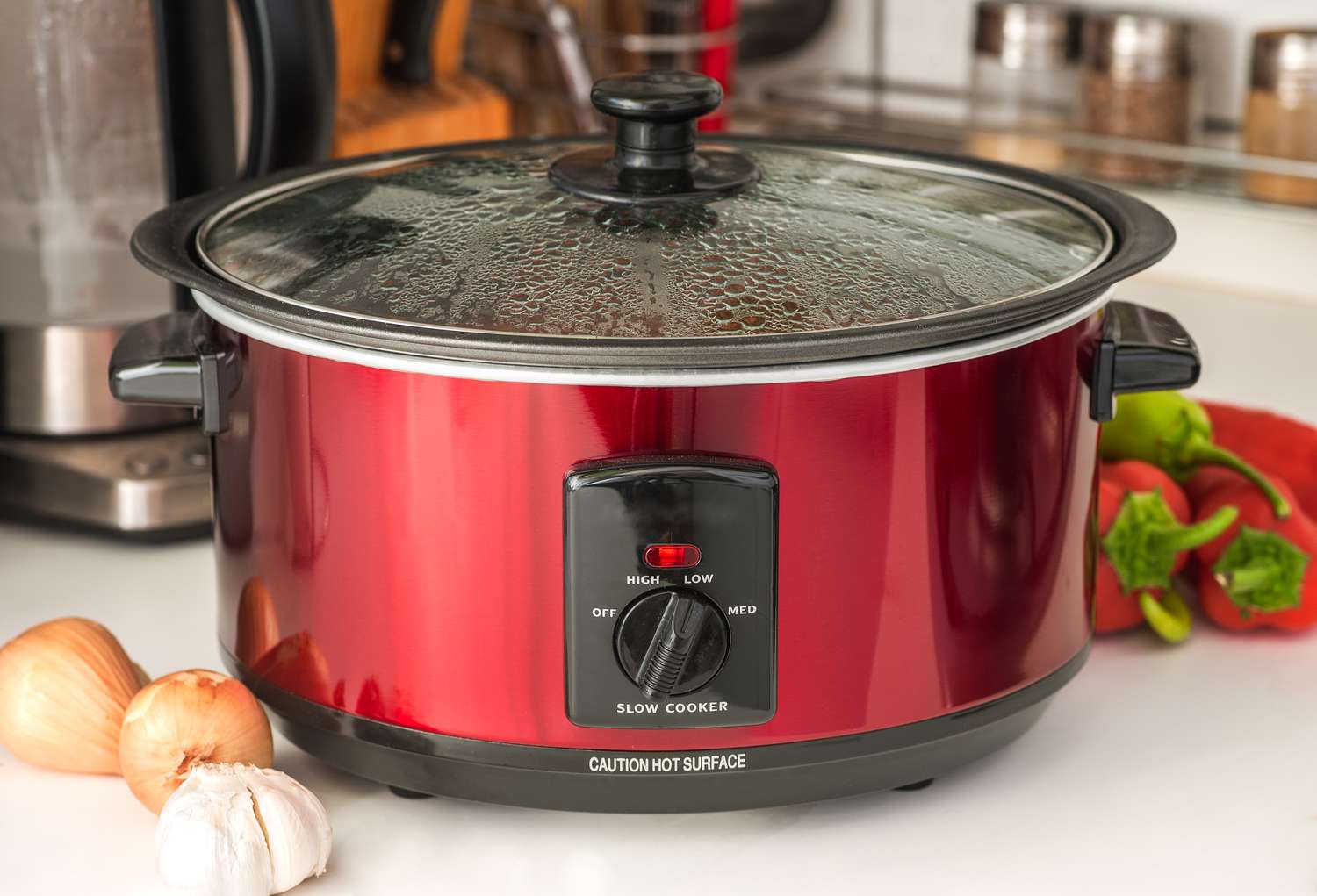 A slow cooker with vegetables and garlic on a countertop