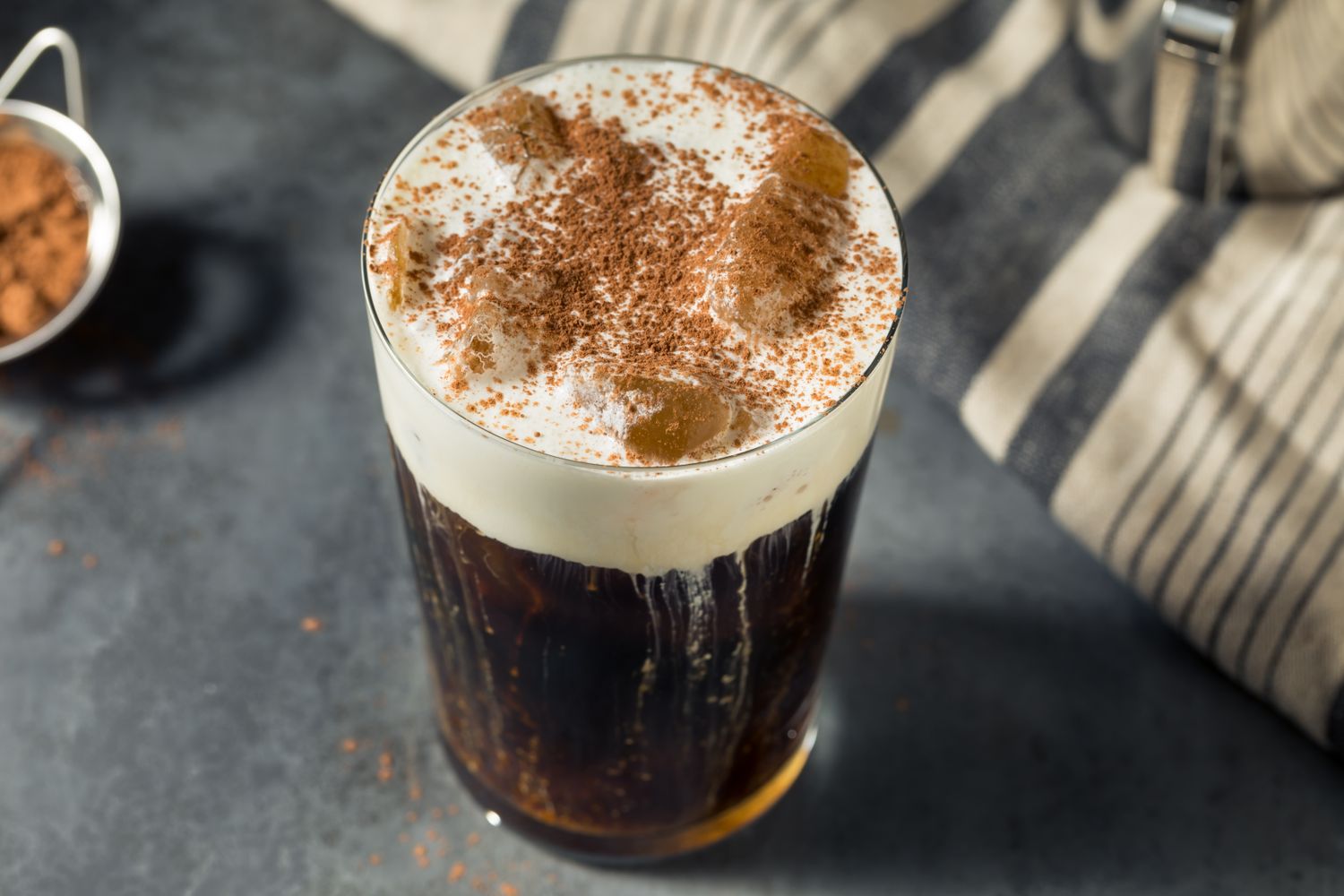 A glass of German iced coffee with whipped cream and cocoa powder on a dark surface