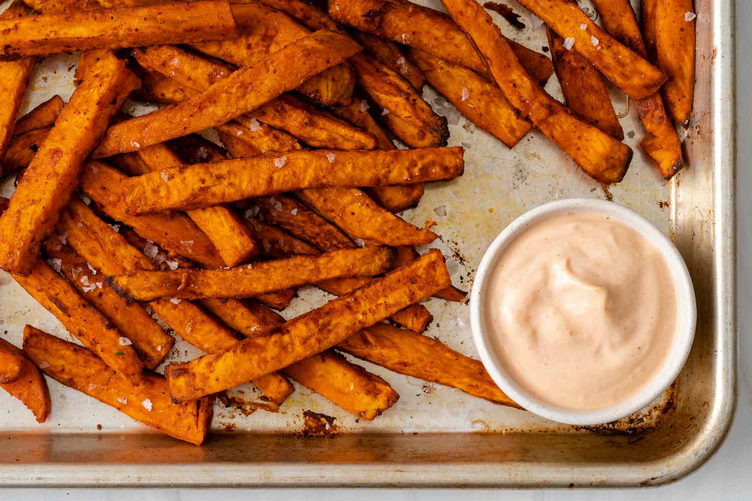 Sweet potato fries on a baking sheet with a dipping sauce