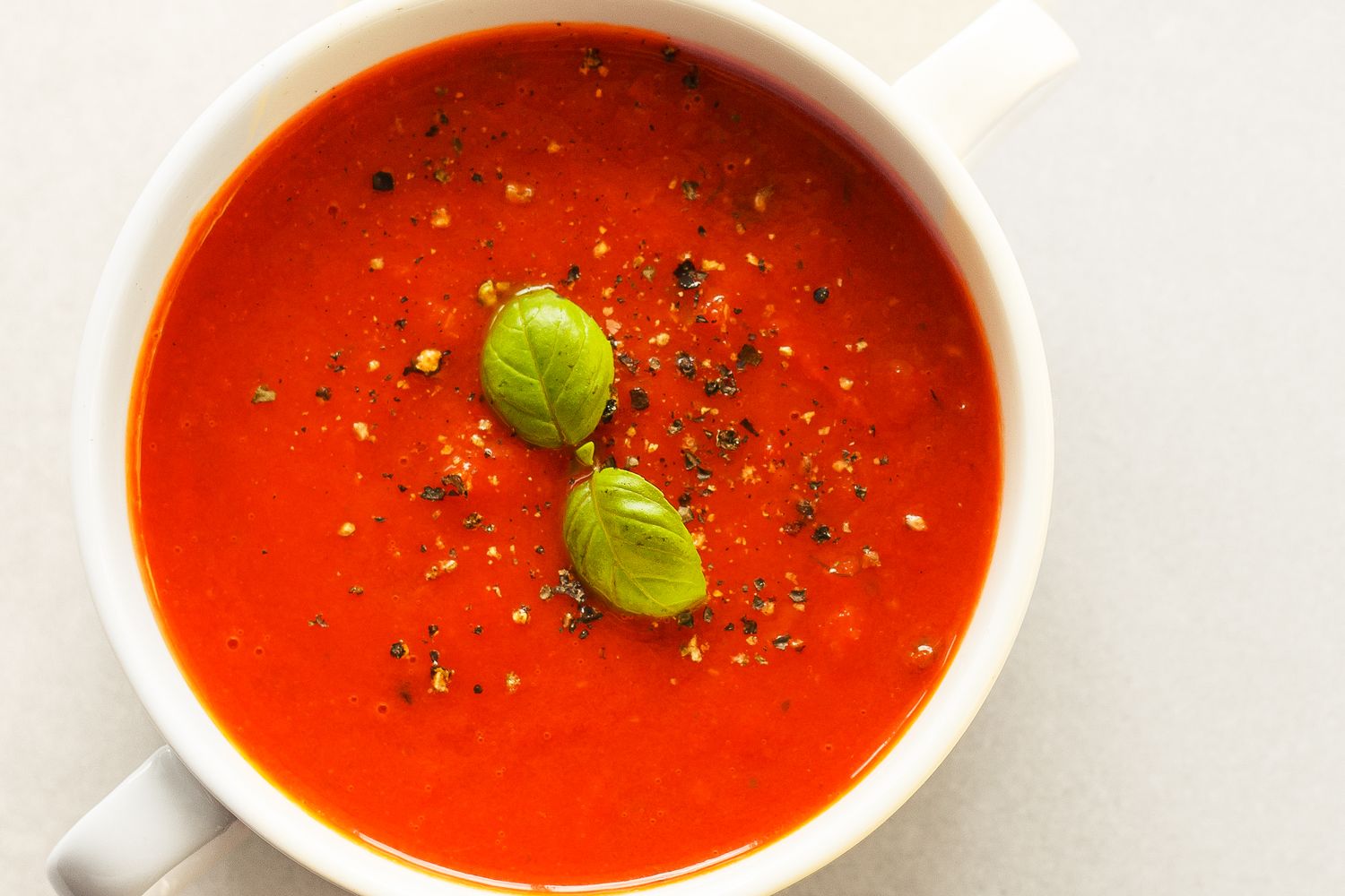 Bowl of tomato soup garnished with basil leaves and black pepper