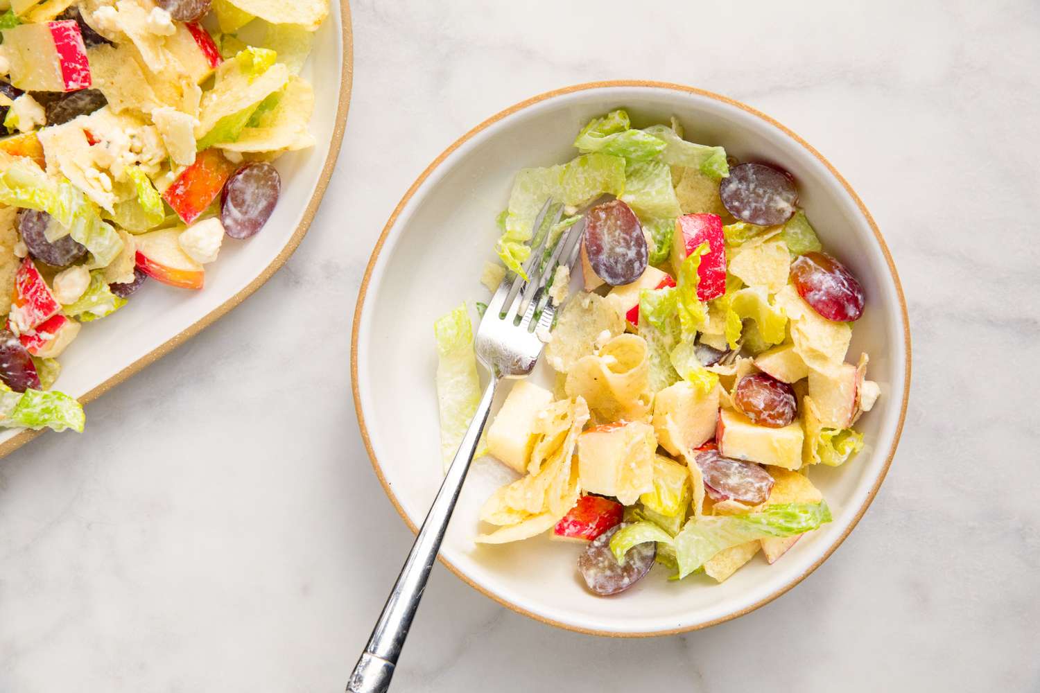 A bowl of salad with lettuce, grapes, and cheese, accompanied by a fork