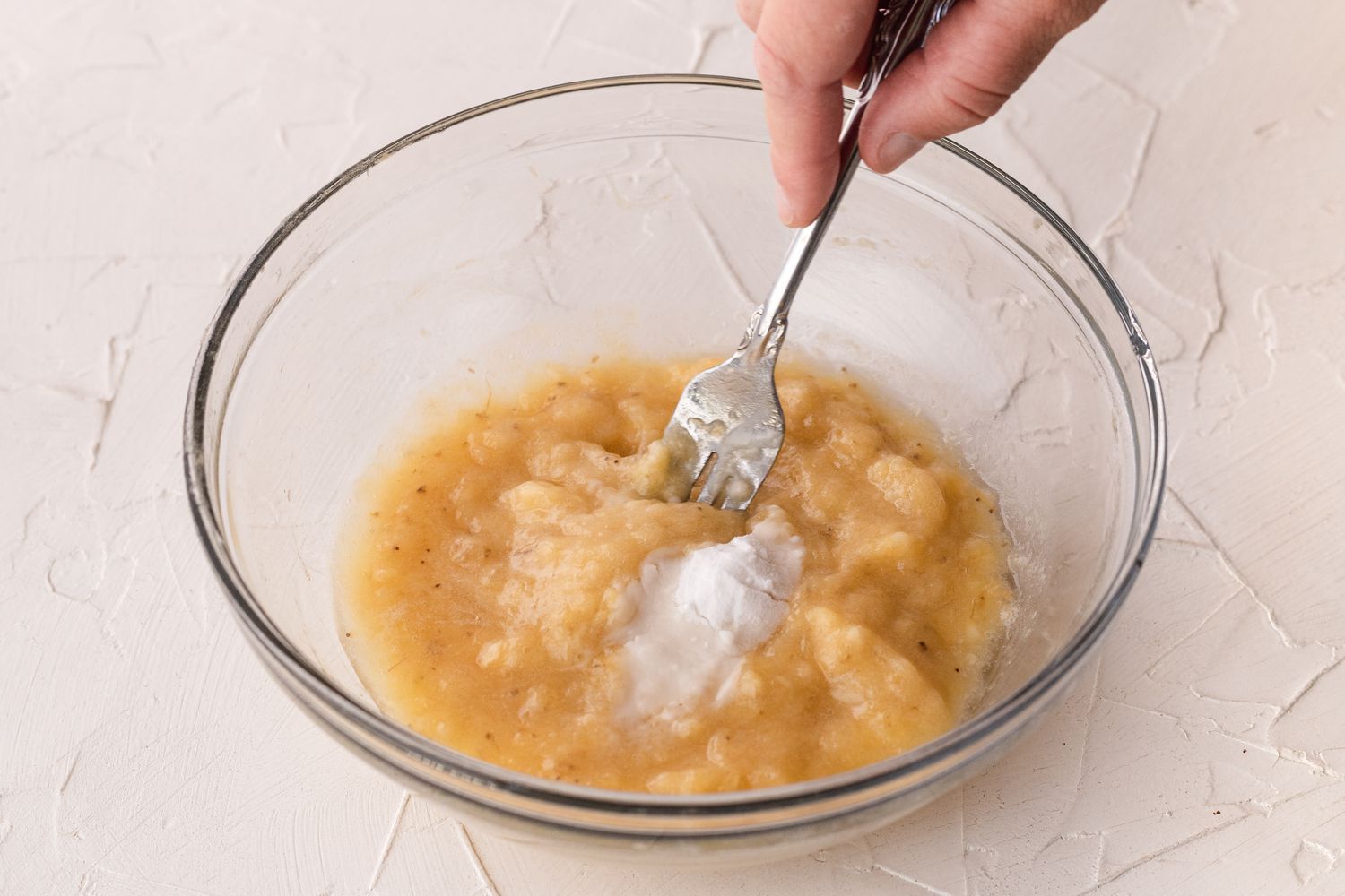 Mashing bananas with a fork in a glass bowl to make a banana cookie recipe.