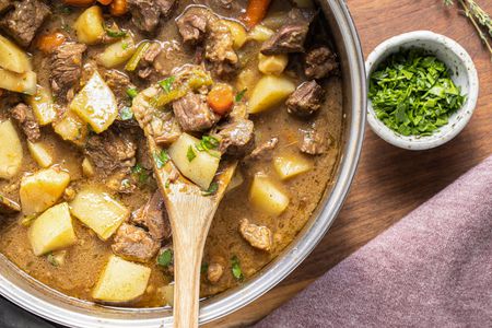 Pot of Easy Beef Stew with a Wooden Spatula, a Small Bowl of Parsley, a Sprig of Thyme, and a Kitchen Towel
