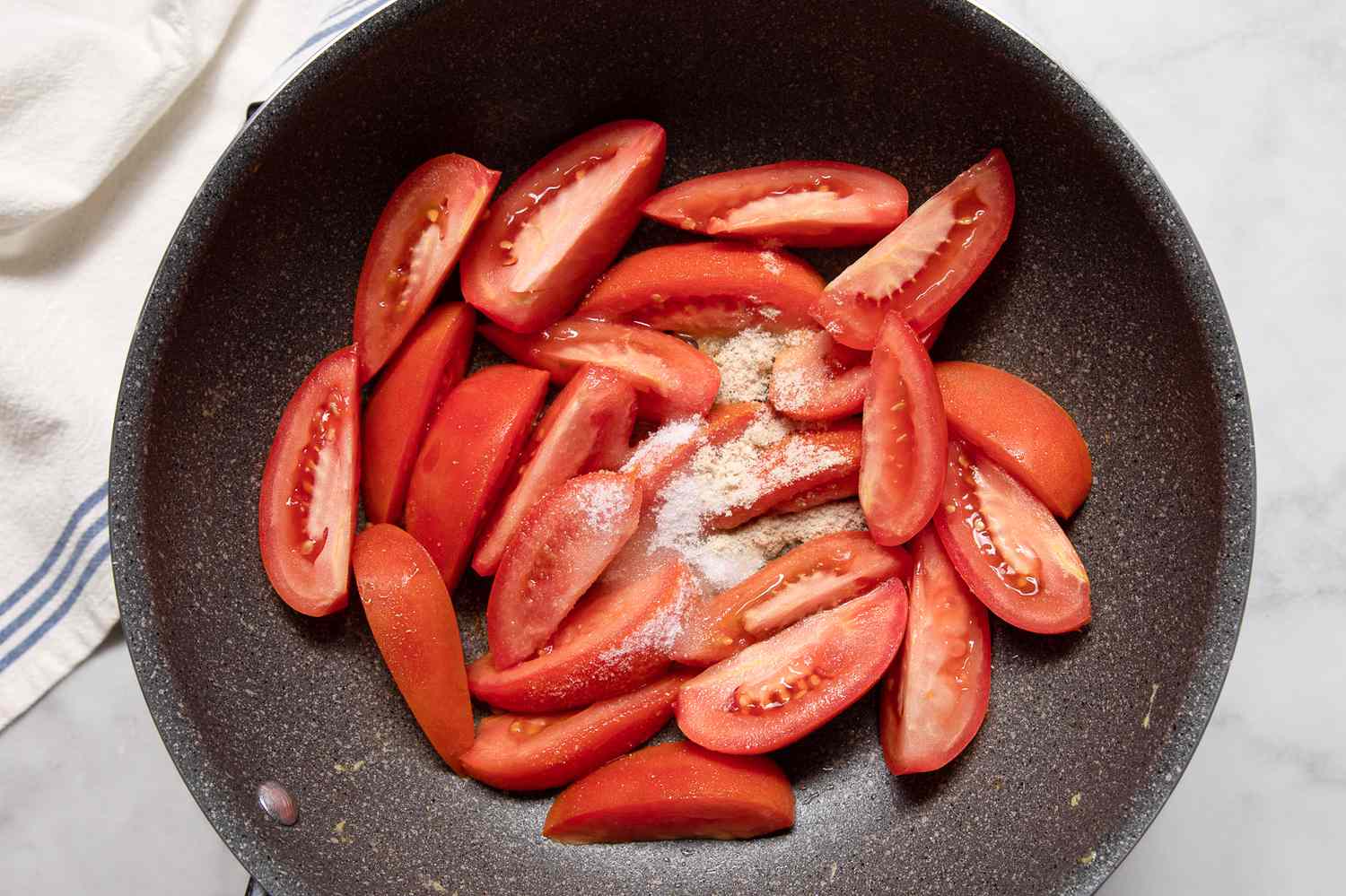 A nonstick skillet with raw tomatoes, salt, and white pepper
