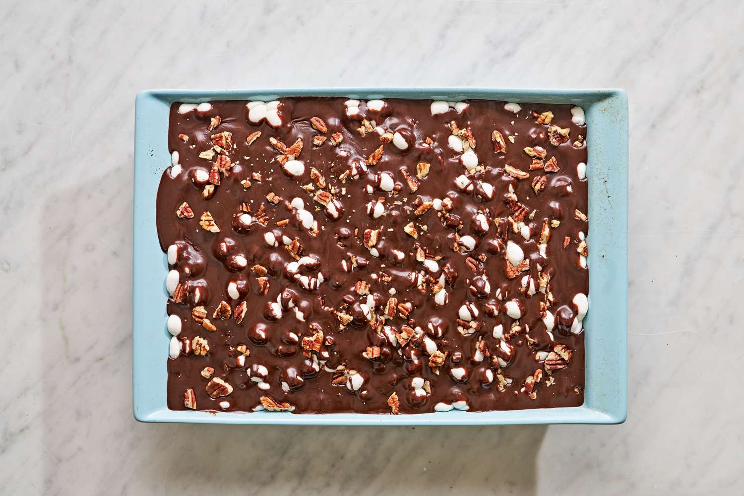 Overhead view of a light blue baking dish of Mississippi Mud Cake recipe after pouring the icing on top of the pecans and marshmallows