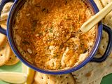 A casserole dish of baked lobster dip with bread crumb topping beside crackers and a lemon wedge