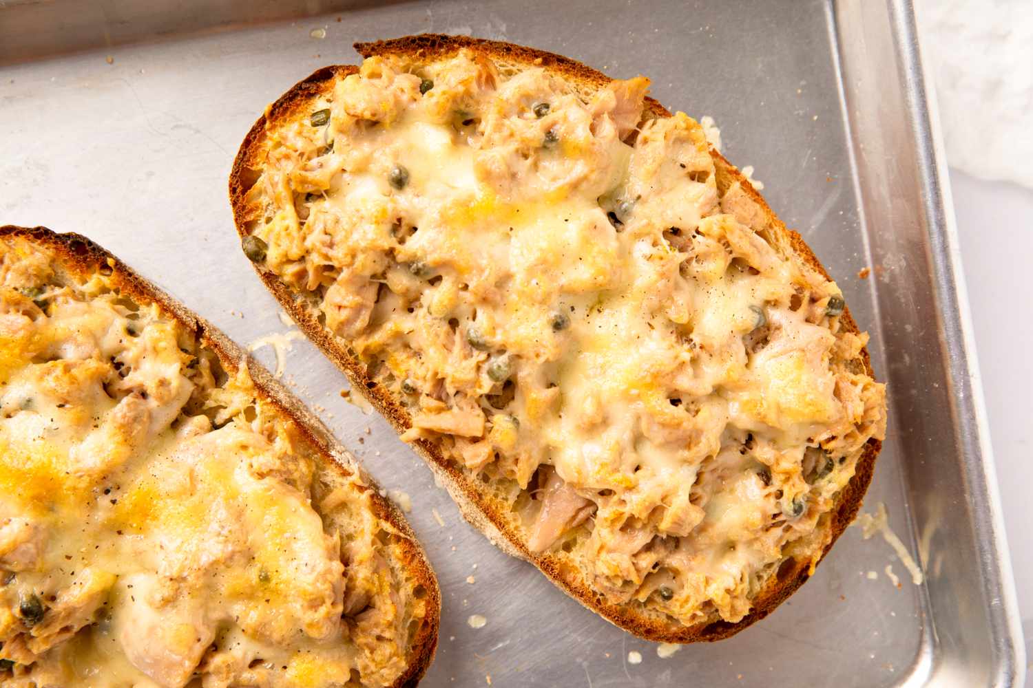 Toasted bread slices topped with a mixture of tuna and melted cheese on a baking tray