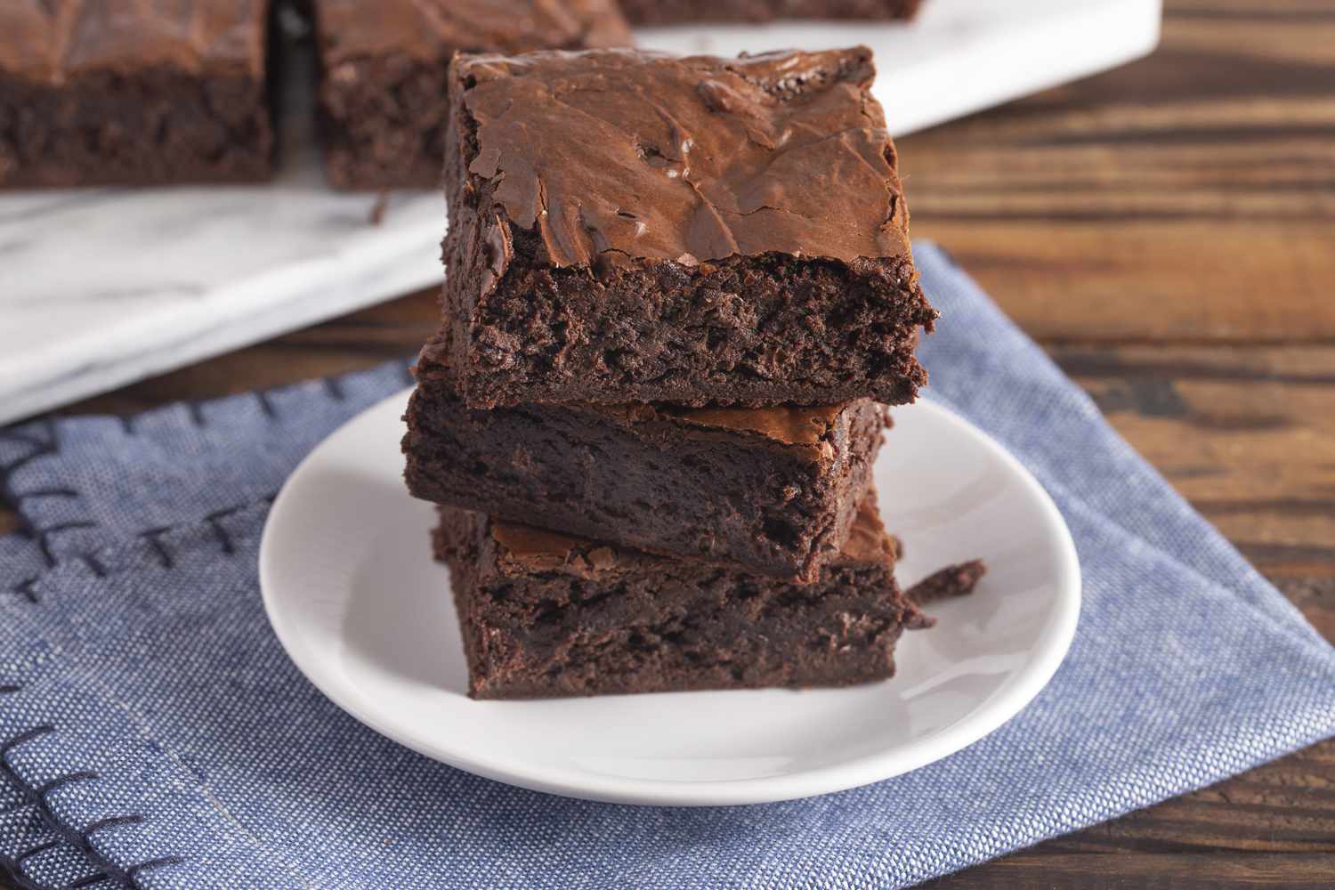Stack of homemade double chocolate brownies on a saucer on top of a blue cloth napkin